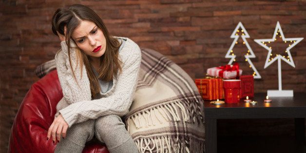 Sad young woman with Christmas presents at her home