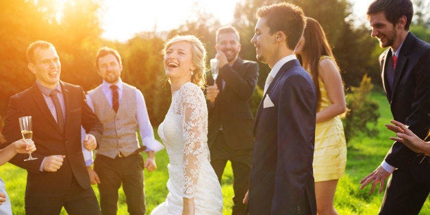 Full length portrait of newlywed couple dancing and having fun with bridesmaids and groomsmen in green sunny park