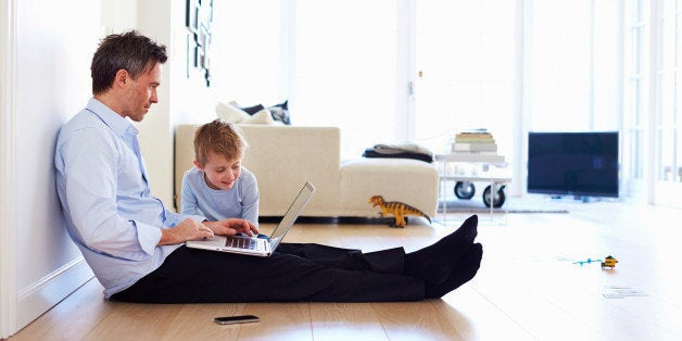 Man sitting on floor using laptop, son watching