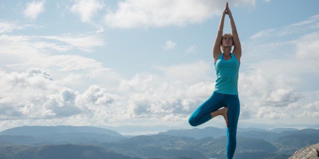 Young woman practicing yoga high up on top of mountain Ulriken, in Bergen, Norway, overlooking mountain range - tree pose or Virksasana.