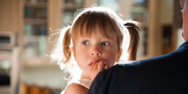 Young girl in pigtails with big brown eyes looks with concern over her father shoulder.