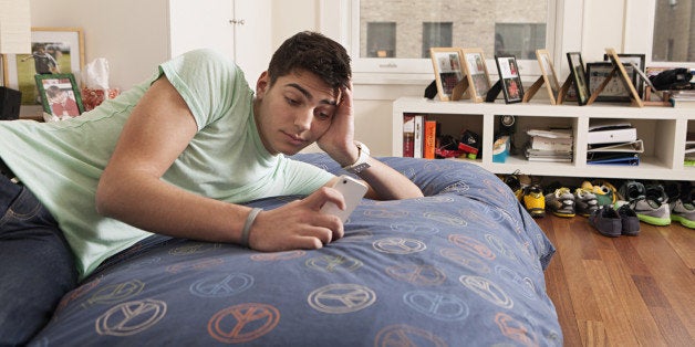 Teenage boy laying on bed looking at a smart phone