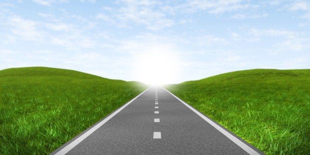 Open road highway with green grass and blue sky with an asphalt street representing the concept of journey to a focused destination resulting in success and happiness.