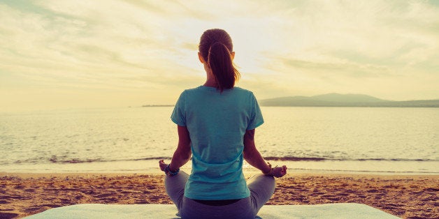 Young woman meditating in pose of lotus on beach near the sea at sunset in summer, rear view