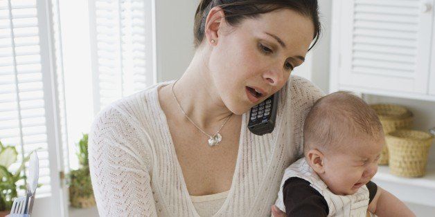 Mother holding baby, talking on telephone and cooking