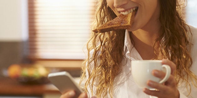 Woman eating breakfast and using phone at home.