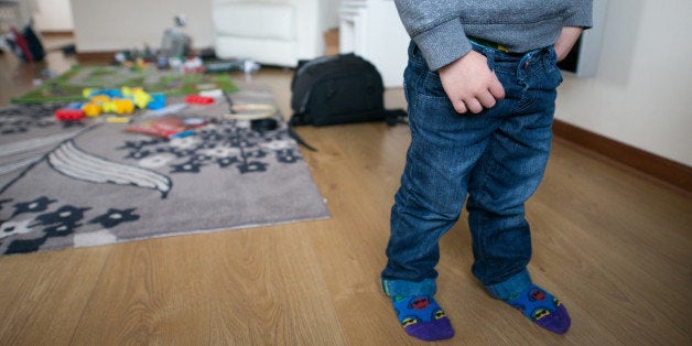 Artistic image of a two year old boy at home with a mess of toys and play things all around him standing.