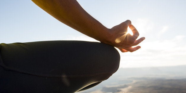 A young woman practicing yoga on top of a cliff at sunset.