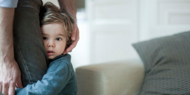 Toddler boy holding on to father's legs