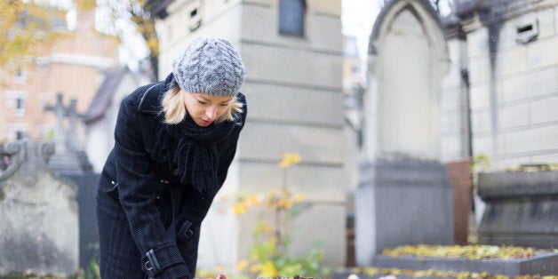 Solitary woman mourning by gravestone, remembering dead relatives in on Pere Lachaise cemetery in Paris, France.