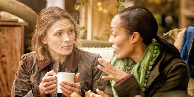 Two female friends discussing over a cup of coffee. They are sitting outdoors in Autumn. Halloween pumpkins can be seen in the foreground.