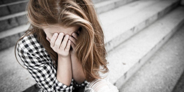 Unhappy depressed teenager with face in hands sitting outdoor