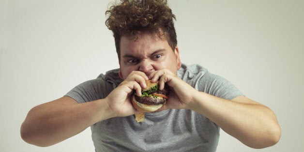 Studio shot of an overweight man biting into a burger