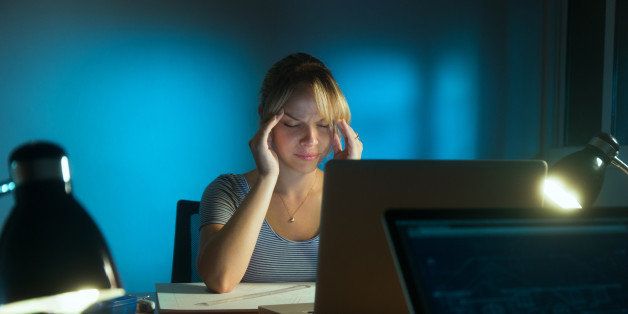Beautiful woman working as interior designer, staying late at night in office with drawings and laptop computer. The girl feels tired and her eyes hurt.