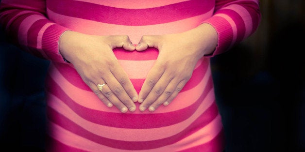 Pregnant woman holding hands on stomach in heart shape.