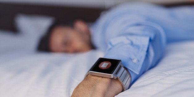 Exhausted businessman sleeping on bed while getting an e-mail on his smartwatch.