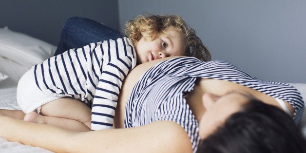 Little girl and pregnant mother lying together on bed