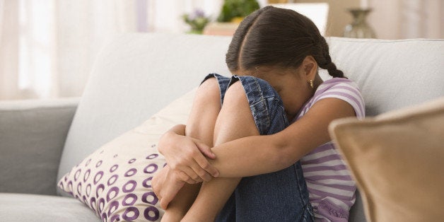 Sad Hispanic girl sitting on sofa
