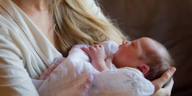 A new mother cradles her newborn infant in her arms, gazing at the 2 day old baby.