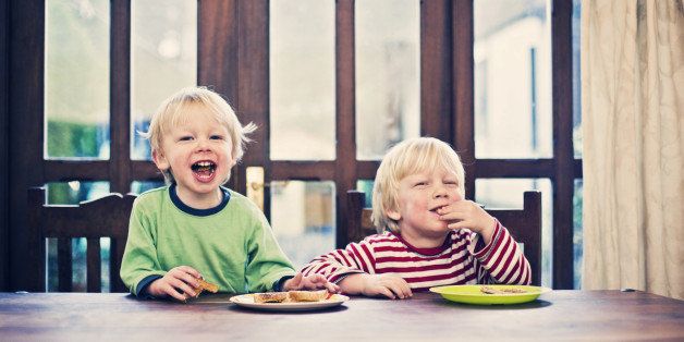 Two happy smiling little brothers sat at breakfast table eating toast.