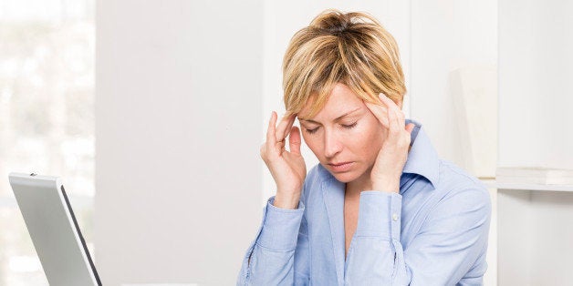 Mature businesswoman with pain in head sitting in her office.