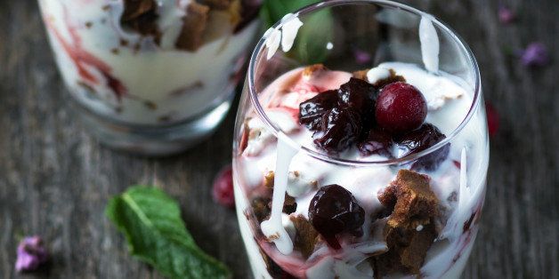 Two glasses with parfait: layered dessert with greek yogurt, cherry compote, cranberries and crumbled brownie. Rustic wooden table background, low key image