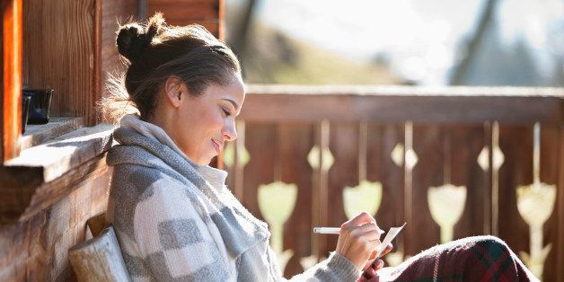 Smiling woman with paper and pen on cabin porch