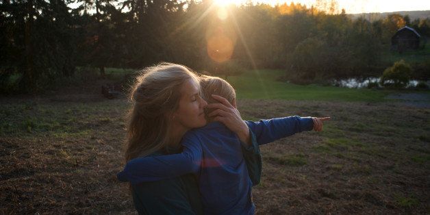 Mother holds son on grassy hill at sunset.