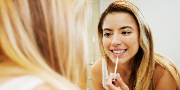 Caucasian woman applying makeup in bathroom mirror