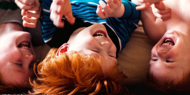 Three brothers hanging upside down off a bed together.