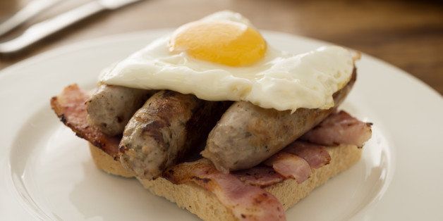Indulgent open breakfast sandwich, bacon, sausages, topped with a fried egg.