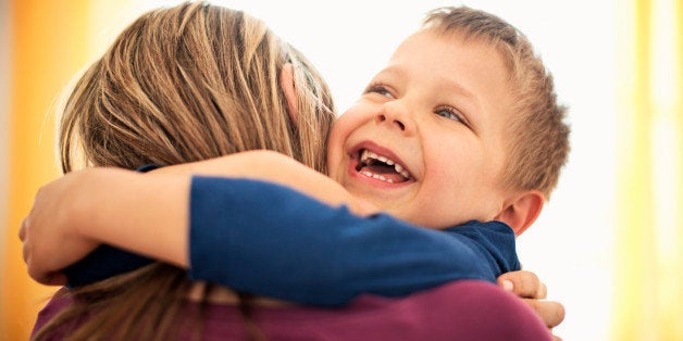 Close up portrait of mother and son hugging. The boy is laughing with joy and both ar backlit by the sunlight coming from the window behind them.