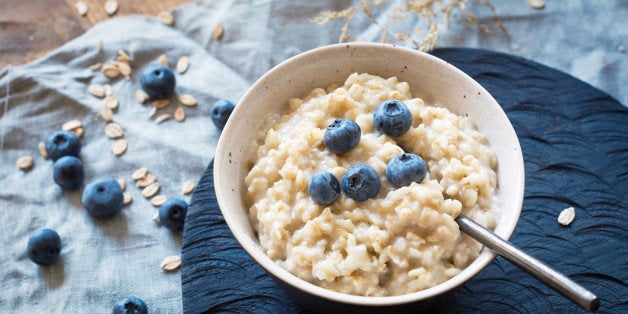 Bowl of oatmeal with blueberries on rustic dark chopping board.