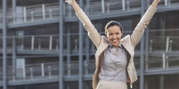 Excited young businesswoman with arms raised standing against office building