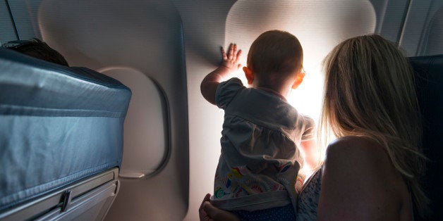 A baby looking out airplane window with her mother.