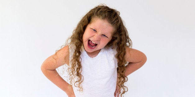 A young girl (aged 8 years) with her hands on her waist and with her mouth wide open shouting with an expression of stress, anger and frustration.