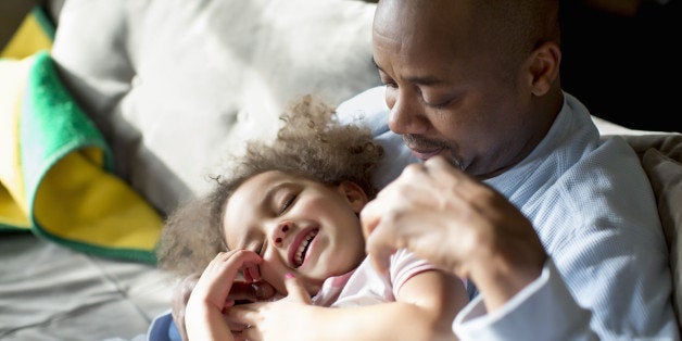 Dad tickling laughing daughter on couch