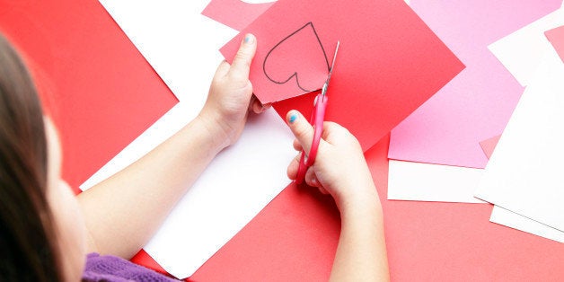 A young girl cuts out a paper heart to use for her Valentine's Day card. 