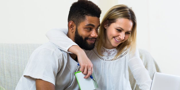 Happy smiling young spouses browsing web and making notes at home