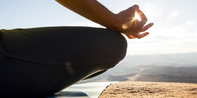 A young woman practicing yoga on top of a cliff at sunset.