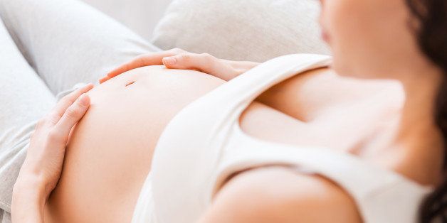 Close-up of pregnant young woman in white tank top touching her belly