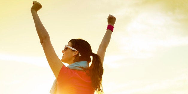 Happy successful sportswoman raising arms to the sky on golden back lighting sunset summer. Fitness athlete with arms up celebrating goals after sport exercising and working out outdoors. Copy space.