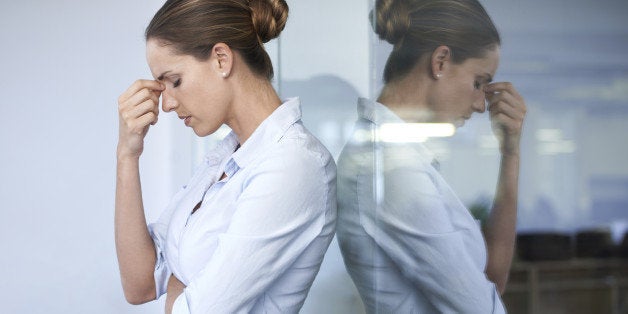 A young businesswoman standing against a glass wall with her head in her hand