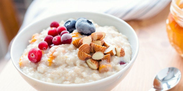 Oatmeal porridge with dried apricots, blueberries, cranberries and chopped almonds on bright wooden table. Jar of honey on background. Selective focus. Bright healthy breakfast image