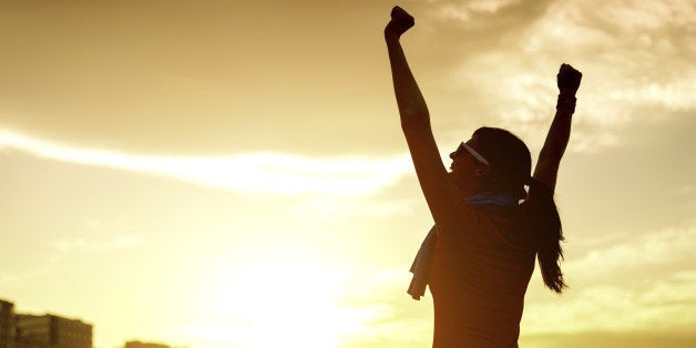 Happy successful sportswoman raising arms to the sky on golden back lighting sunset summer. Fitness athlete with arms up celebrating goals after sport exercising and working out outdoors. Copy space.