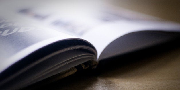 An open hardback picture book, on a pine-coloured desk, in soft focus.