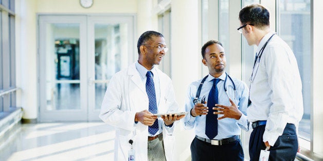 Smiling doctor holding digital tablet in discussion with two colleagues in hospital corridor