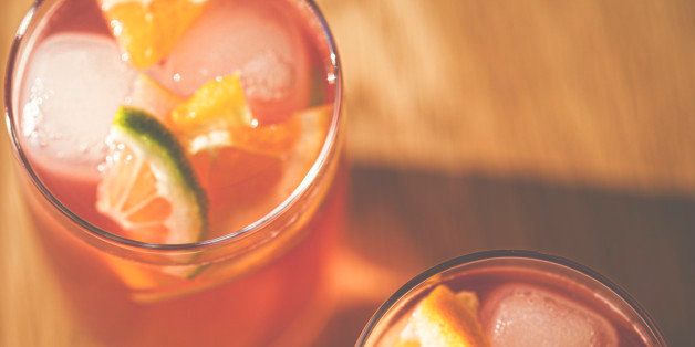 Top down view of 2 glasses of fruity punch with ice cubes and slices of lime and orange.