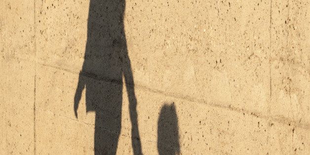 A Child being lead away by a women. there shadows reflected on a wall.