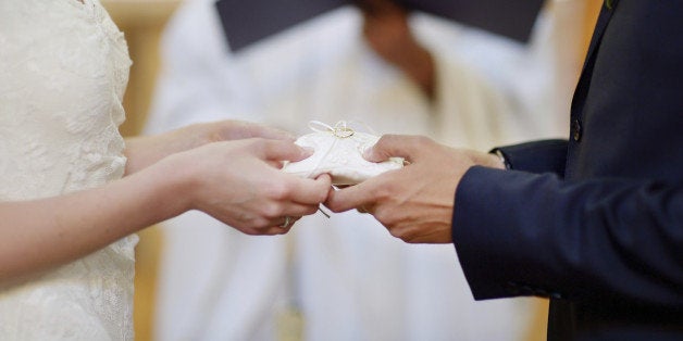 Bride and groom's hands holding wedding rings on a pillow